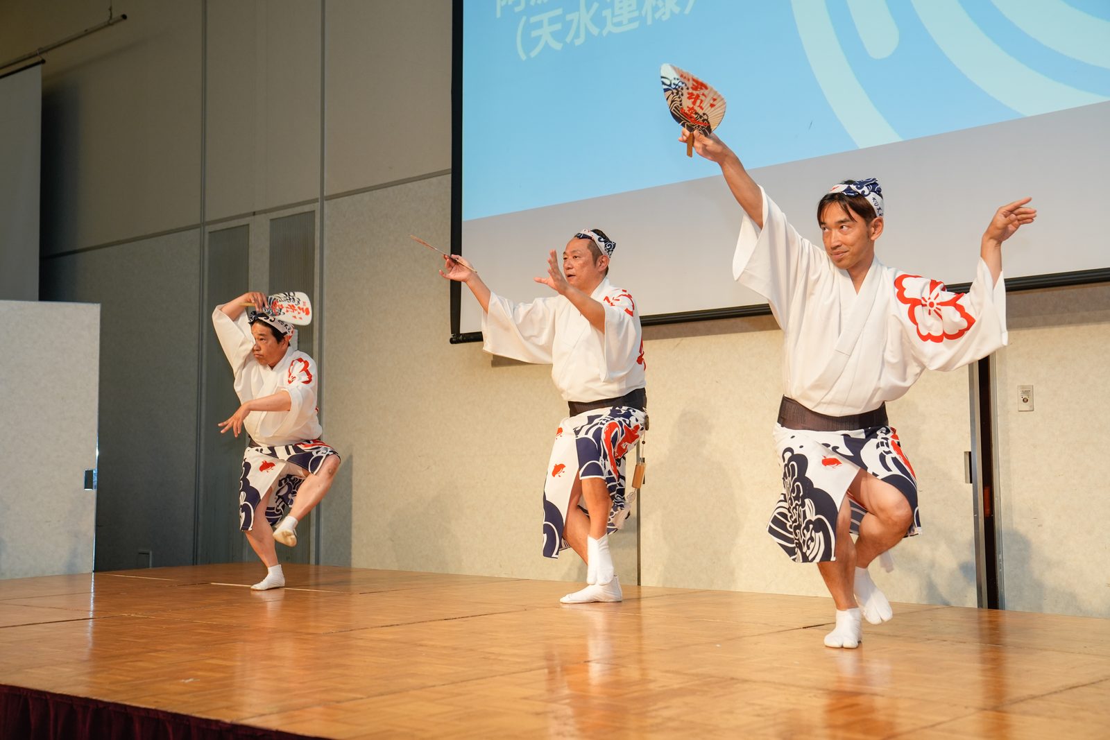 舞台の上で、白い襦袢に鉢巻き姿の踊り手3名が阿波踊りを披露している様子