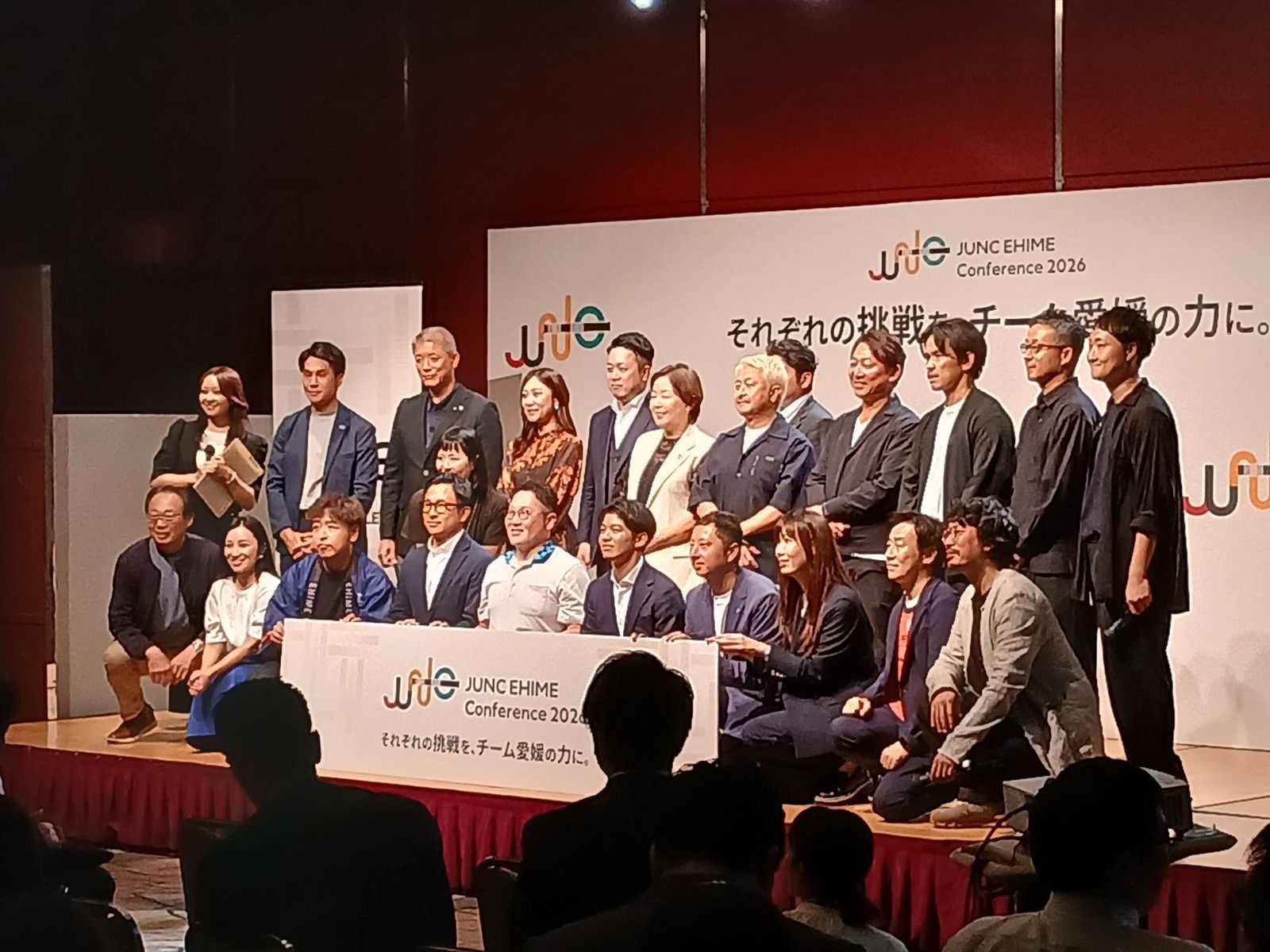 JUNC EHIME Conference 2026のパネルを前に、壇上に並んだ大勢の集合写真