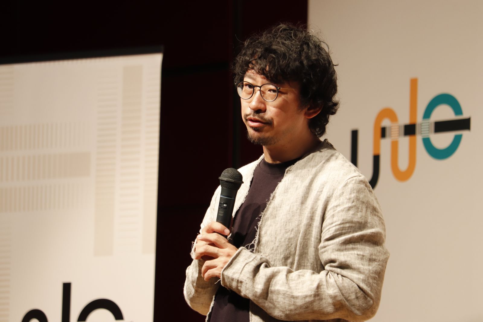 JUNCのロゴを背に、マイクを持って話す登壇者