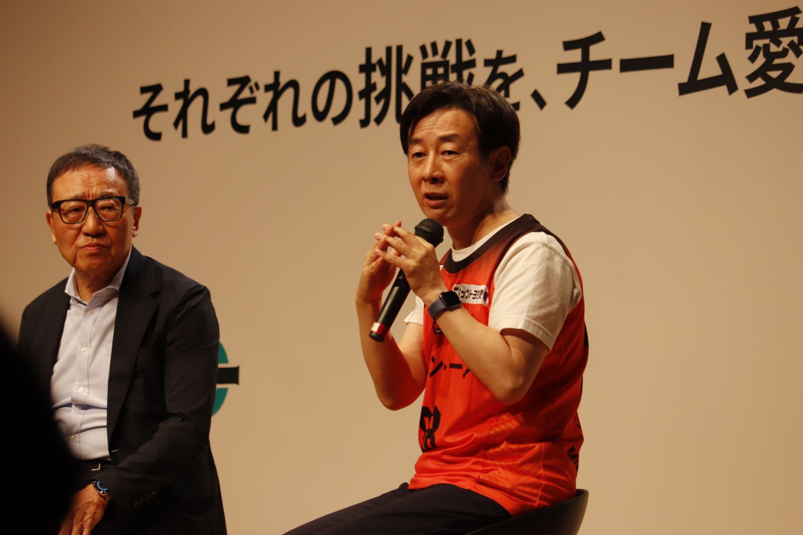 「それぞれの挑戦を、チーム愛媛の力に。」と書かれたボードの前で、マイクを手に話す登壇者