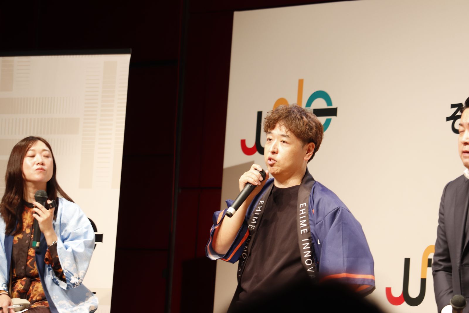 EHIME INNOVATION BASEの文字が入ったたすきを掛け、マイクを持って話す登壇者